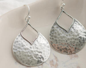 Close-up of sterling silver pear-shaped hammered dangle earrings with French hook ear wires on a marble surface.

